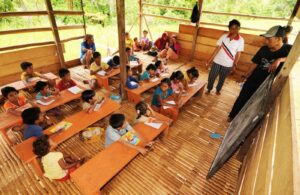 Guru mengajar siswa di ruang kelas sederhana sebagai simbol perjuangan akses pendidikan di daerah tertinggal Indonesia.