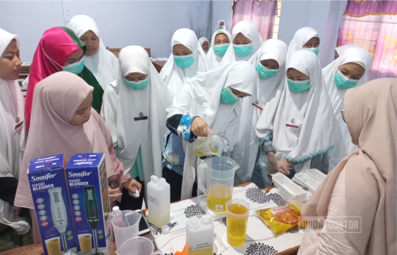 “Santriwati Gontor Putri Kampus 3 mengikuti pelatihan pembuatan sabun padat; dosen TIP UNIDA Gontor membimbing proses pencampuran bahan dengan APD di Laboratorium, terlihat cetakan dan peralatan sabun di meja.”