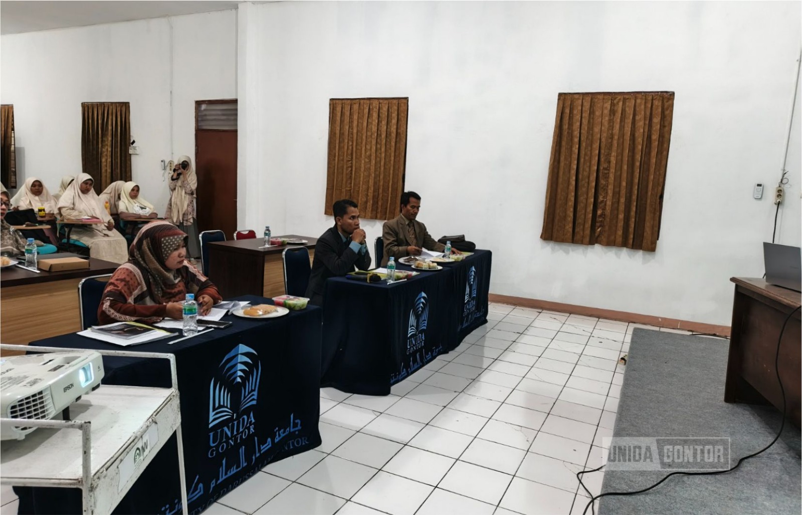 Sidang Skripsi Perdana Fakultas Syariah UNIDA Gontor di Aula CIOS Beirut Kampus Gontor Putri 1, mahasiswi HES mempresentasikan penelitian di hadapan dosen penguji.