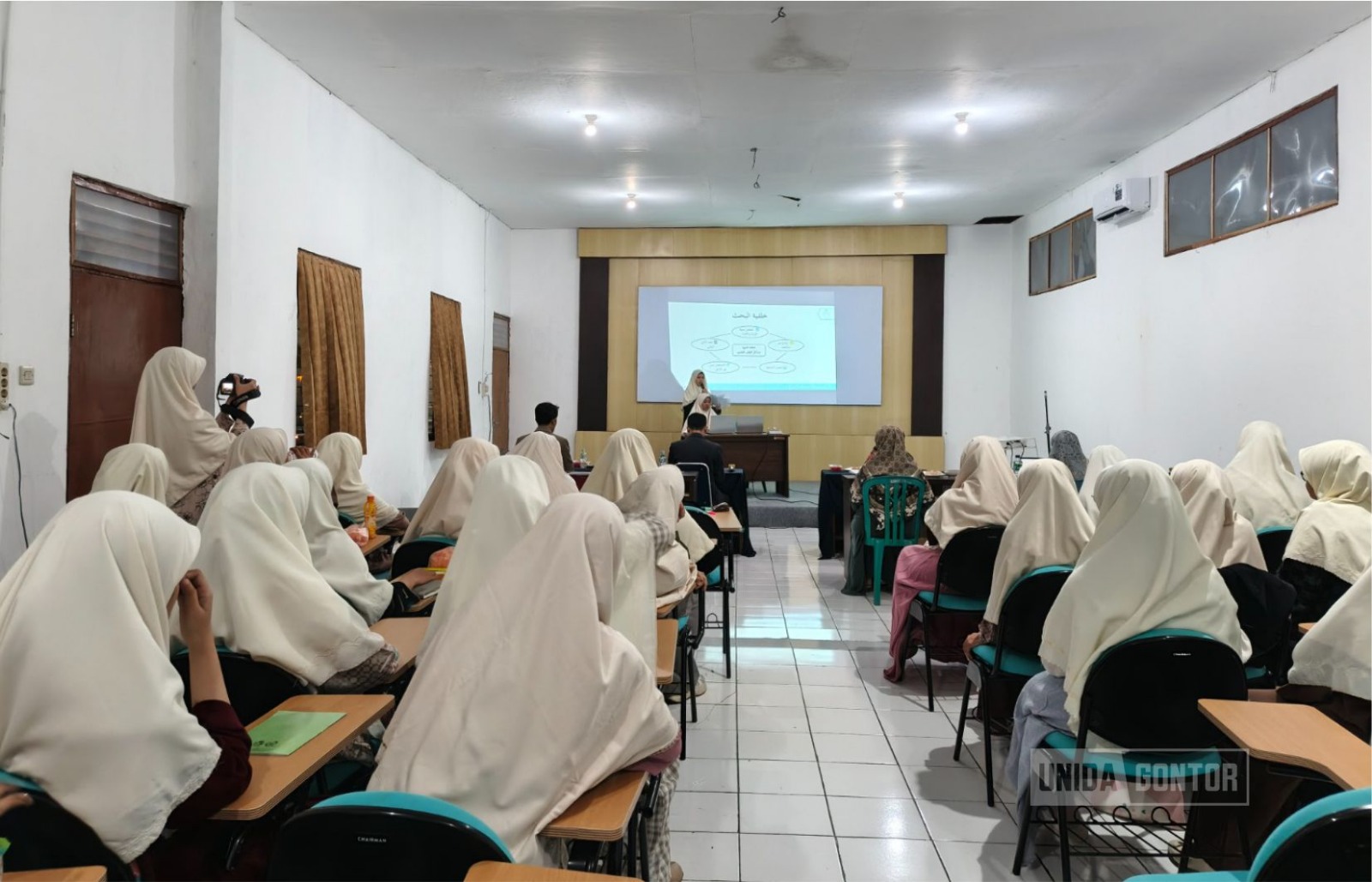 Sidang Skripsi Perdana Fakultas Syariah UNIDA Gontor di Aula CIOS Beirut Kampus Gontor Putri 1, mahasiswi HES mempresentasikan penelitian di hadapan dosen penguji.